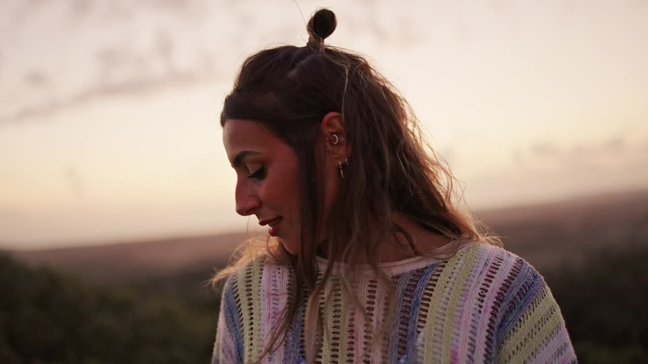 Woman with long hair in a top knot looking down at sunset