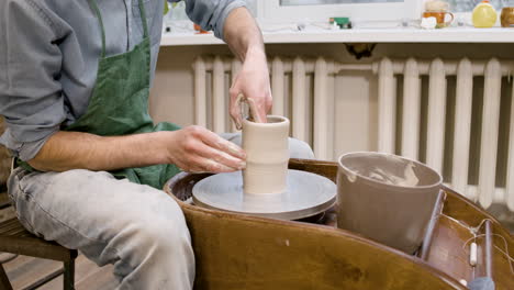 close up view of clerk in green apron modeling ceramic piece on a potter wheel in a workshop 1