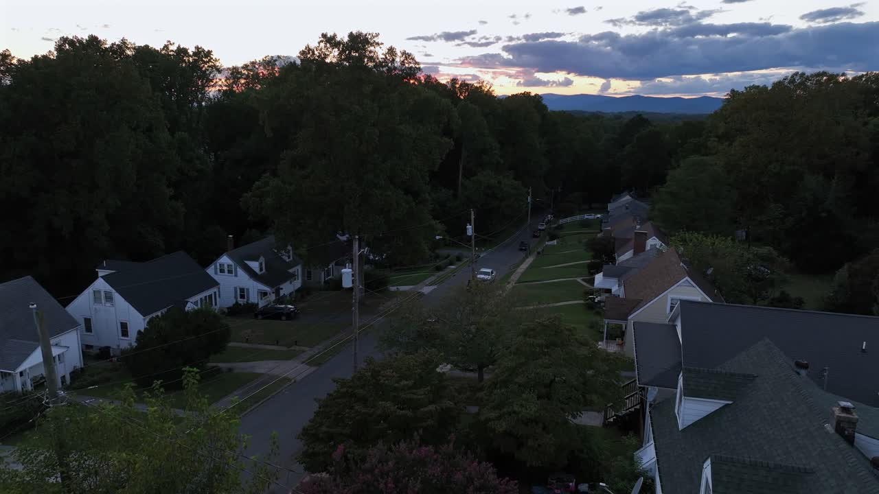 Classical american one family houses with porch and parking cars on road. Suburb district with green trees during golden hour. Descend drone wide shot. Pathway, driveway and front yards of property