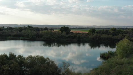 Drohnenaufnahme-Eines-Sees-Mit-Wolken,-Die-Sich-Auf-Dem-Wasser-Und-Dem-Wald-Am-See-Spiegeln