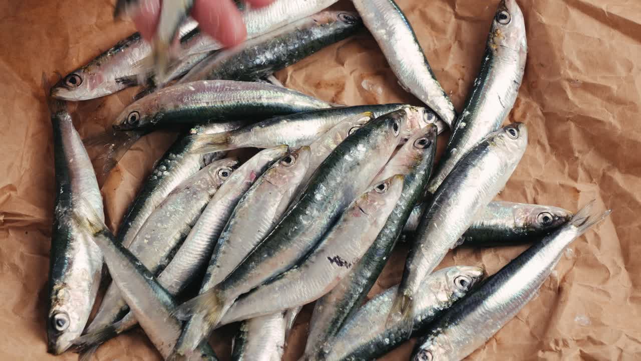Hand touching sardines on brown paper