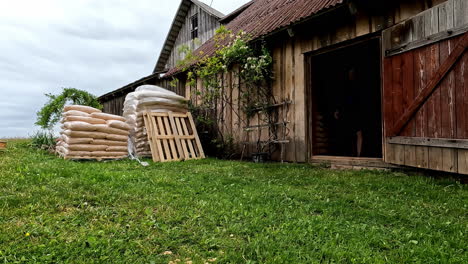 Man-taking-bags-of-material-into-wooden-farm-building,-time-lapse