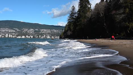 Small-blue-waves-of-water-rooling-on-the-brown-sandy-beach-while-white-foam-returning-to-the-sea-while-people-walking-around