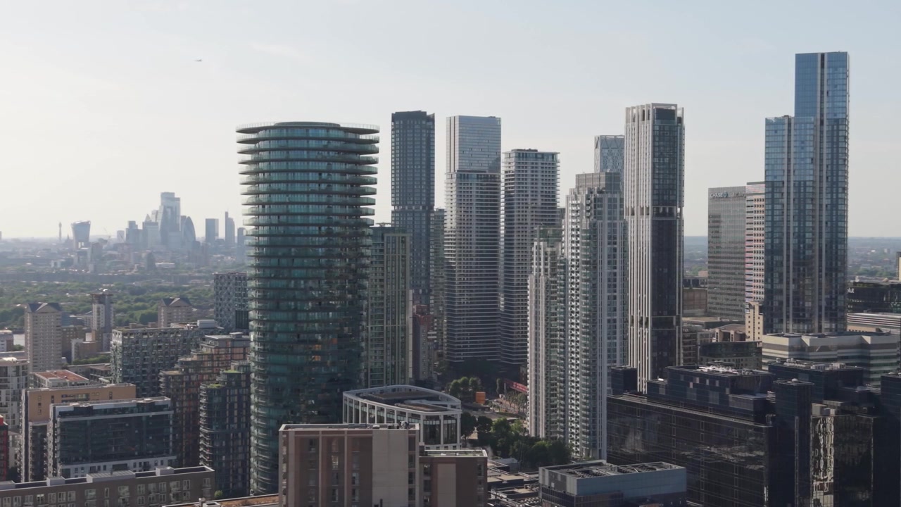 Vista panoramica di una città vivace dall'alto, con numerosi grattacieli di vetro che si ergono verso il cielo azzurro e limpido. La luce del sole illumina l'ampio paesaggio urbano.