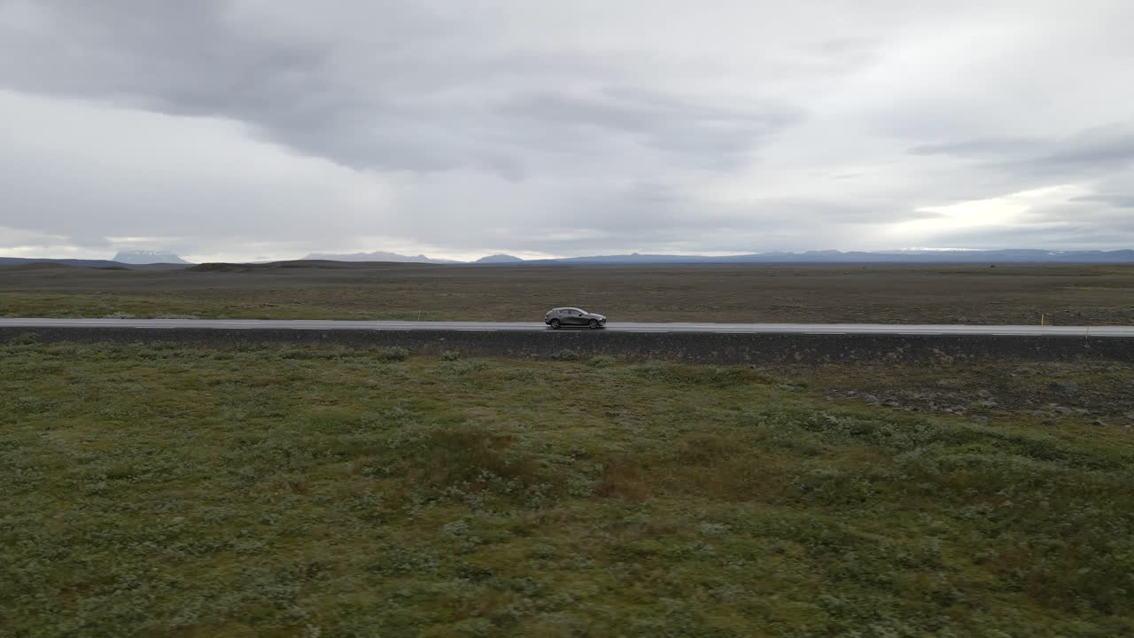 Driving a car through Iceland's vast plains with a 4K drone following a car amidst endless dirt and distant mountains