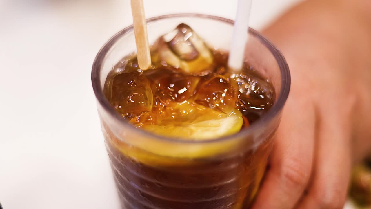 Mano che mescola tè freddo con una fetta di limone