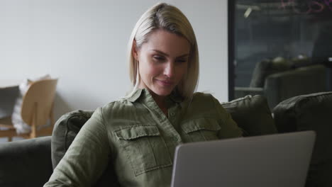 caucasian businesswoman sitting on couch using a laptop in modern office