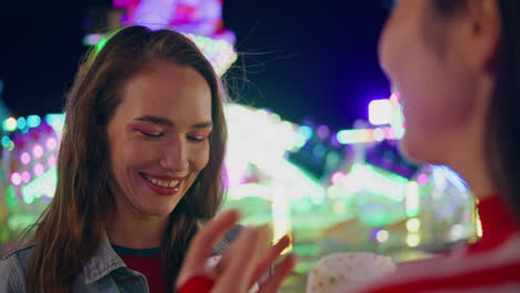 una amiga sonriente hablando en una feria iluminada de primer plano. una adolescente descansa.