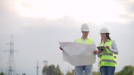 Coworking-engineers-with-tablets-on-solar-plant.-Adult-men-and-women-in-hardhats-using-tablets-while-standing-outdoors-on-transformer-platform.-Transportation-of-clean-energy.-Wind-energy-delivery