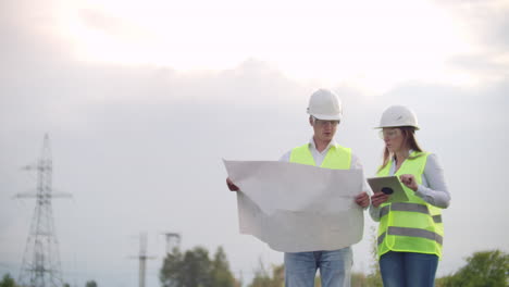 ingenieros de coworking con tabletas en la planta solar. hombres y mujeres adultos con cascos usando tabletas mientras están al aire libre en la plataforma de transformadores. transporte de energía limpia. entrega de energía eólica
