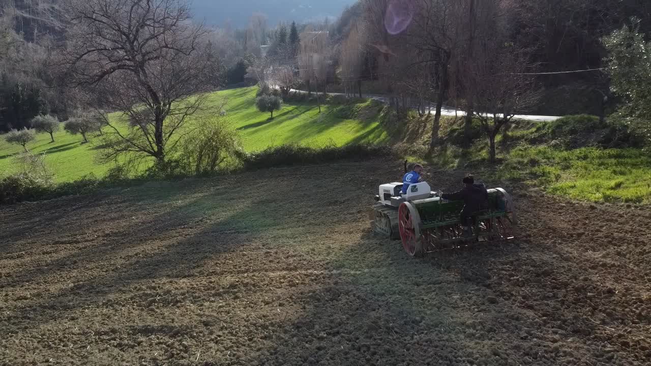 farmer on tractor with seeder sowing the land at sunset, aerial shot