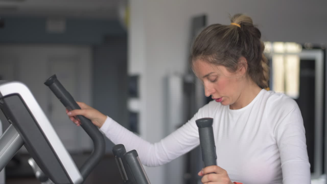 Woman in white activewear working out on the elliptical machine at the gym