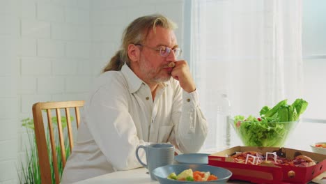 man sitting at table looking sad while eating