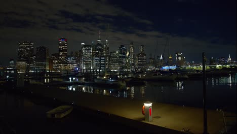 tomada amplia de los muelles del puente de brooklyn por la noche con el horizonte de nueva york en el fondo y barcos amarrados