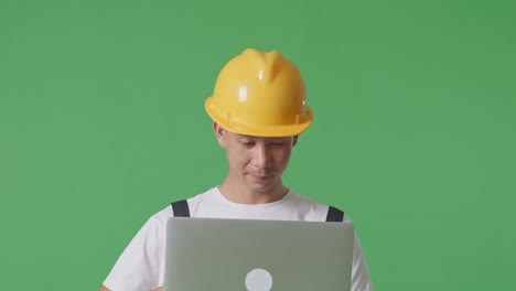 close up of asian man painter wearing safety helmet using a laptop while standing in the green screen background studio