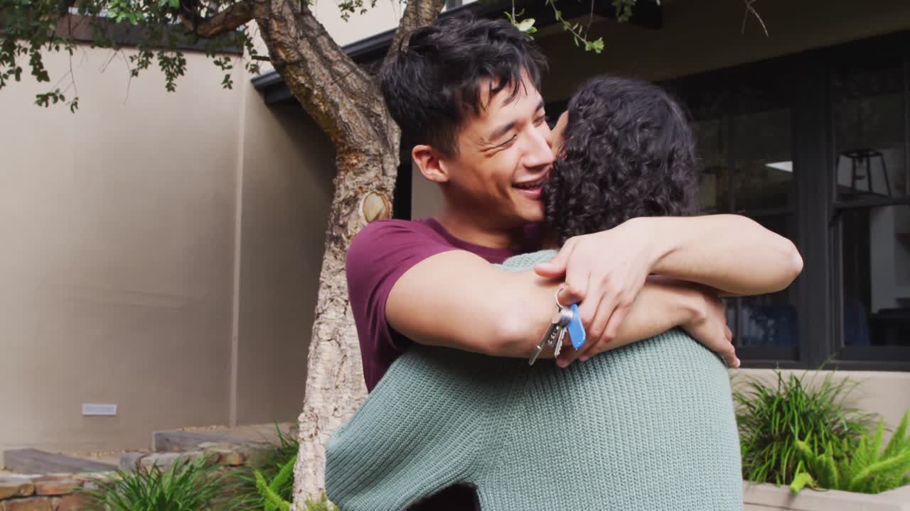 hombre feliz y diverso mudándose de casa, sosteniendo las llaves, abrazándose y sonriendo