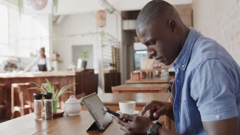 hombre afroamericano usando teléfono inteligente y tableta en una cafetería, cámara lenta