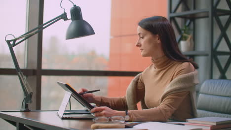 a female graphic designer works in an office with large windows and paints using a stylus and a computer touch screen. workstation with touchscreen for designers. come up with and develop the concept of the logo.