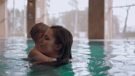 woman and her preschooler son are resting in water park swimming in indoor pool