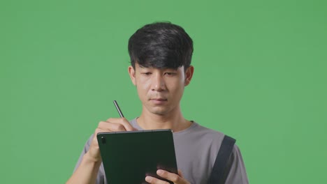 녹색 스크린 배경 스튜디오에서 는 동안 태블릿에 메모를 취하는 아시아인 노동자의 클로즈업