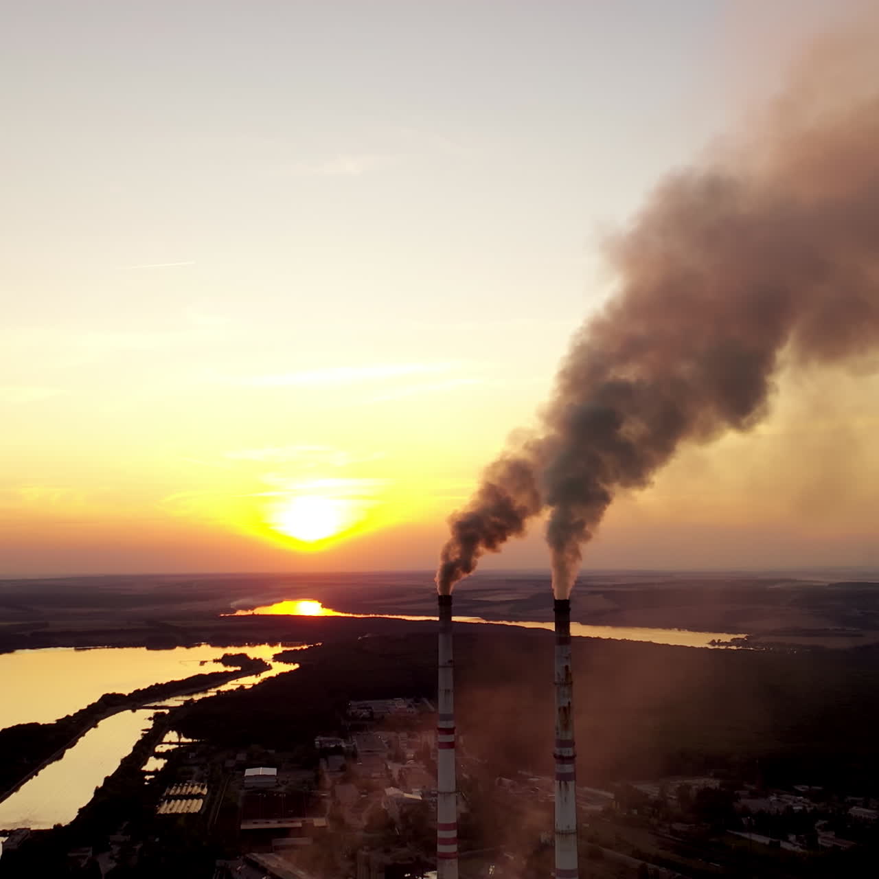 Industrial factory at sunset. Dirty smoke coming from pipes on the nature background in the evening. Manufacture near the river.