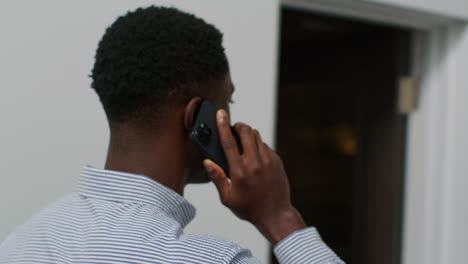 close up of smiling young businessman walking along corridor in office talking on mobile phone 3