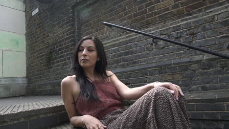 Hispanic-Latina-model-posing-while-sitting-on-stairs-and-looking-around-with-a-floral-dress,-summer-concept-shot