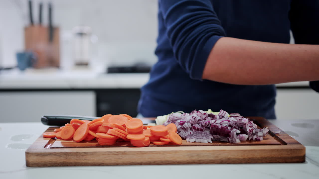 Woman cutting up a red bell pepper near other vegetables on a wooden cutting board