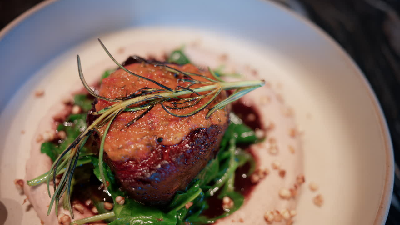 Close up of a gourmet meat dish served with sauce, greens, and rosemary garnish on a white plate