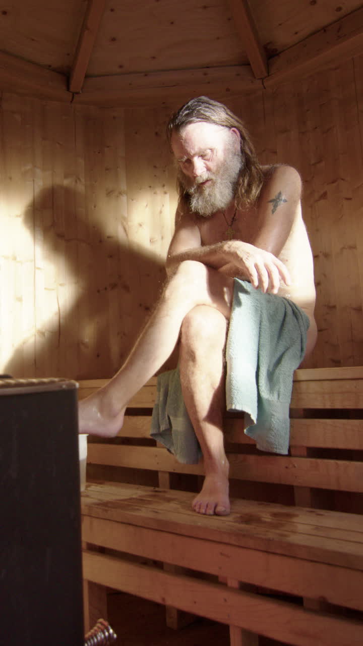 Ungroomed man sit relaxed with crossed legs meditating inside sauna, vertical