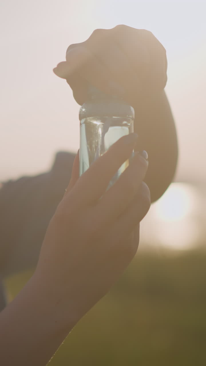 A woman opens a small foaming bottle under the warm sunlight, while a young child eagerly watches beside her, excitement evident on his face. a tender, joyful moment bathed in a golden glow