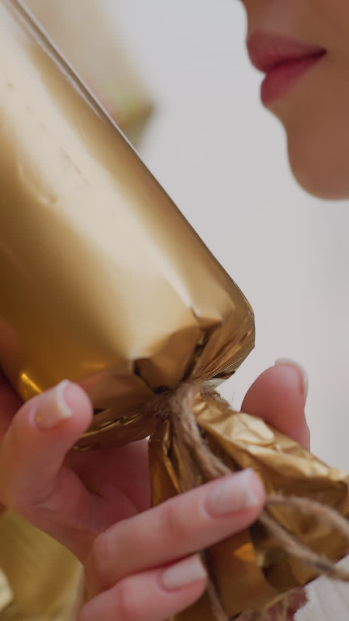 Close-up of woman gently holding Christmas decoration from Christmas tree adorned with golden lights, admiring festive ornament while warm holiday glow reflects on surface in cozy seasonal
