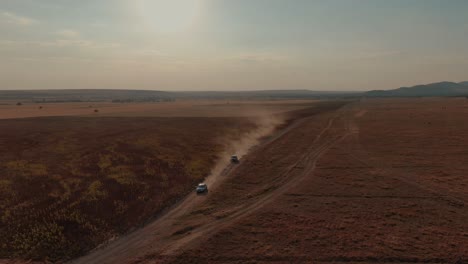 drone shot of two cars driving on a country road between agricultural fields at sunset or sunrise