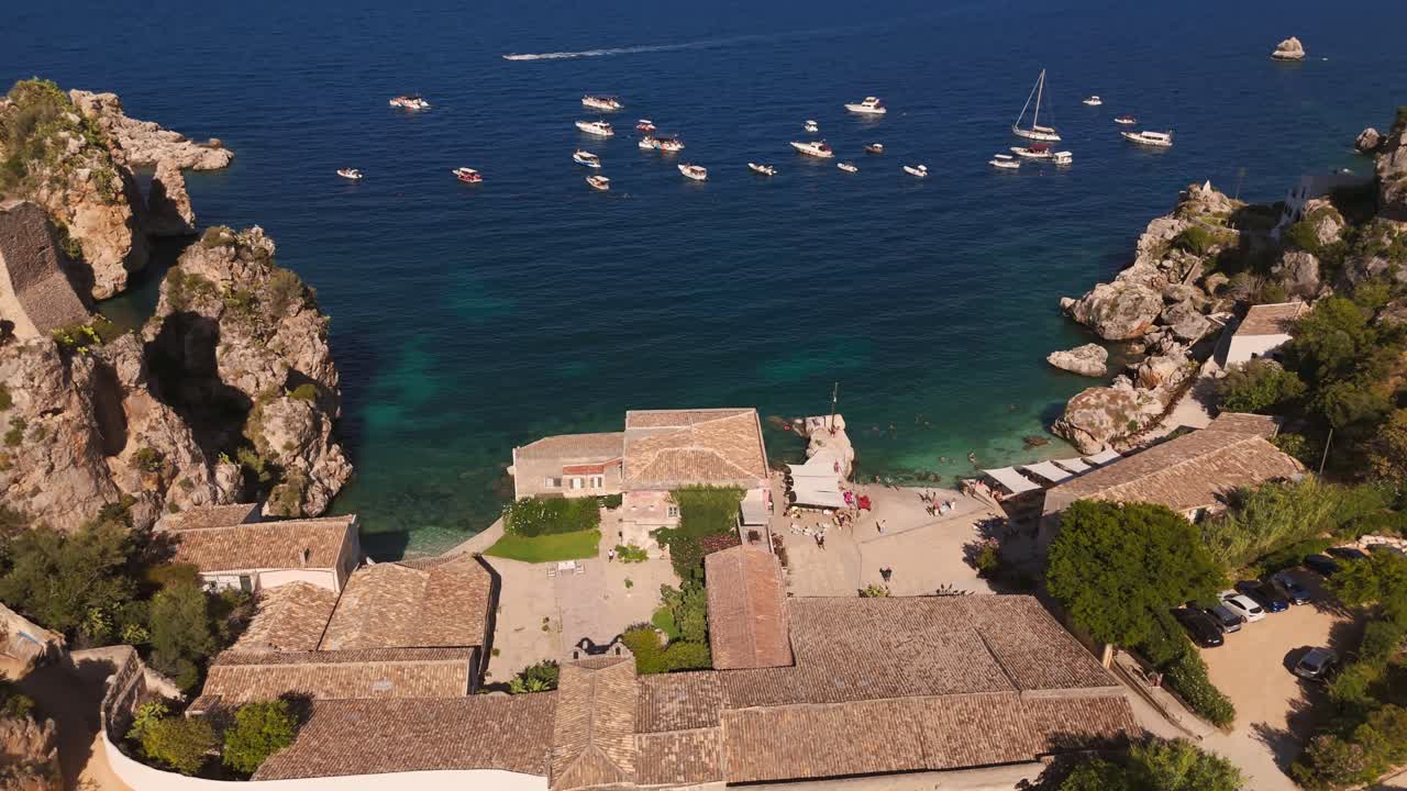 Aerial drone push-in shot revealing Tonnara di Scopello resort and boats on the ocean during Italian summer in Sicily, Italy