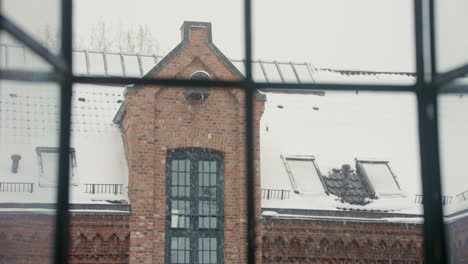 snowflakes drift past a window, framing a historic brick building