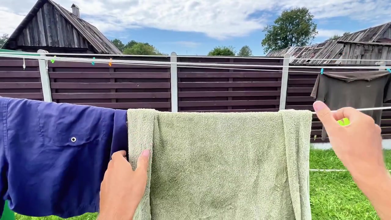 A person hangs a wet towel on an outdoor clothesline using a green plastic clothespin. Ideal for domestic chores, housekeeping, sustainability, and home lifestyle content.