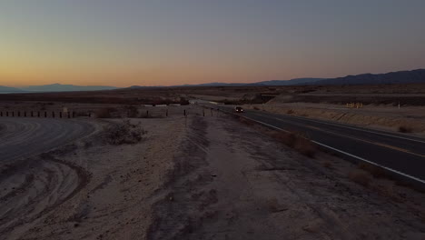 Car-with-Headlights-Drives-along-Interstate-Freeway-Situated-at-Salton-Sea-California-at-Dusk,-Static-Wide-shot