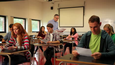 Dozent-Verteilt-Unterlagen-An-Seine-Studenten-Im-Klassenzimmer