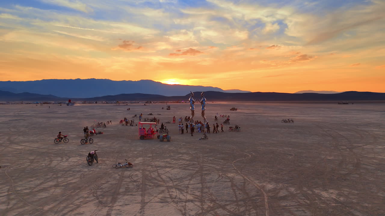 Nevada, USA, 15 August 2025: People gathered around metal statue in desert during vibrant sunset. Silhouetted art installation and people in desert landscape with bright orange sunset