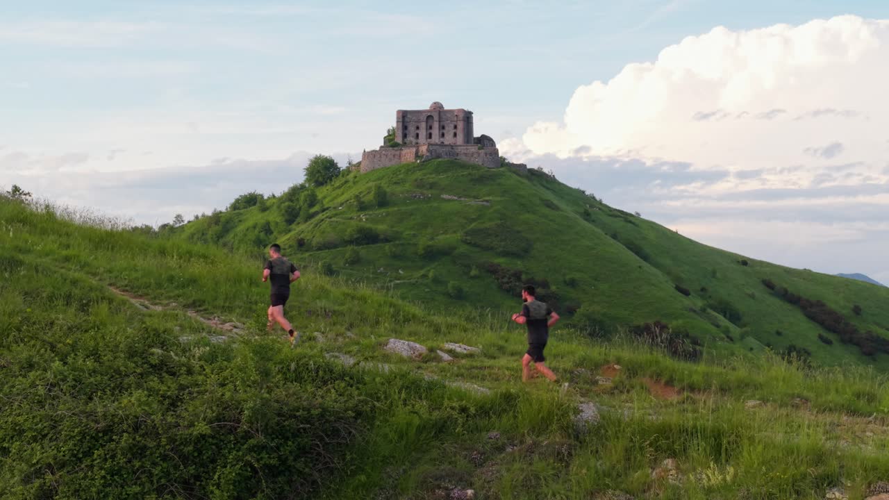 Two people trail running near ancient Italian fort on lush green hill in spring