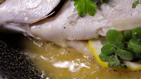 cooking bream fish in a pan with oil, lemon and parsley