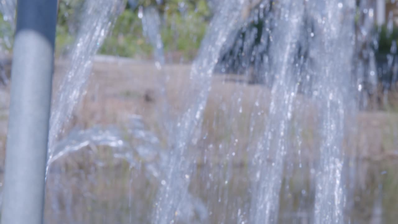A soothing close-up shot capturing the gentle flow of water cascading outdoors, reflecting sunlight in a tranquil setting. Perfect for evoking calm and natural beauty