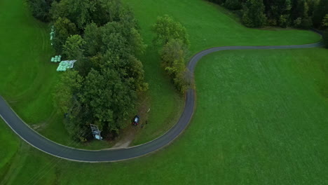 Luftdrohnenaufnahme-Von-Oben-Nach-Unten-über-Eine-Kurvenreiche-Straße,-Die-Tagsüber-Von-Grünen-Wiesen-Umgeben-Ist