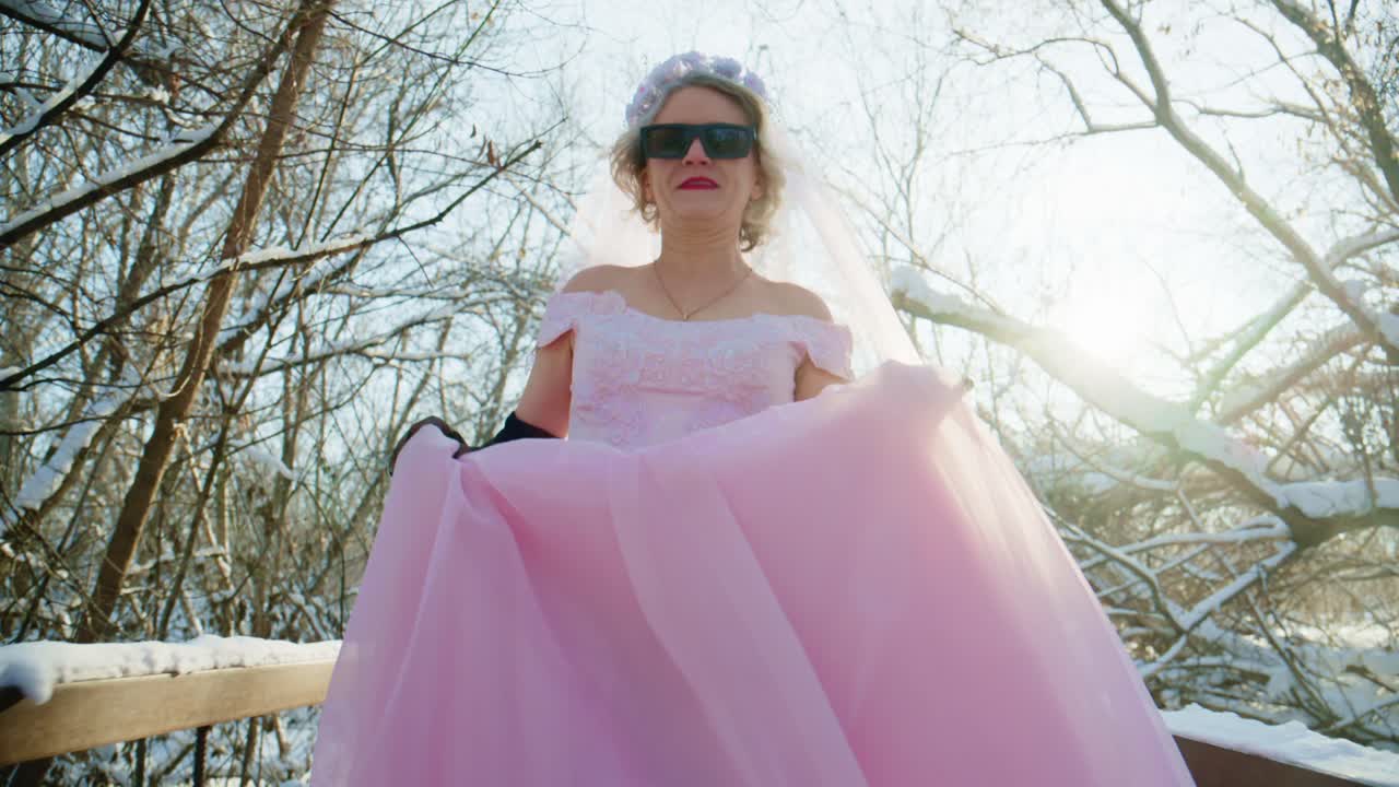Sposa felice in abito da sposa rosa che posa in una foresta innevata.