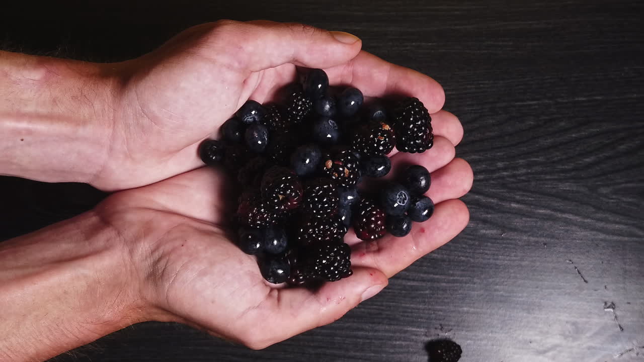 Overhead slowmotion shot of falling blueberries on the hand of a young man in front of a black background