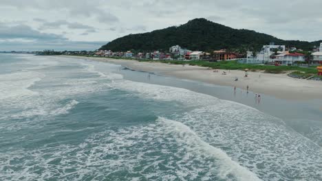 Luftaufnahme-Eines-Bevölkerten-Sandstrandes-In-Der-Nähe-Des-Meeres-Und-Der-Stadt,-Brasilien-Im-Sommer