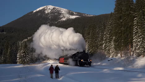 historic steam train traversing a snowy mountain forest with winter hikers