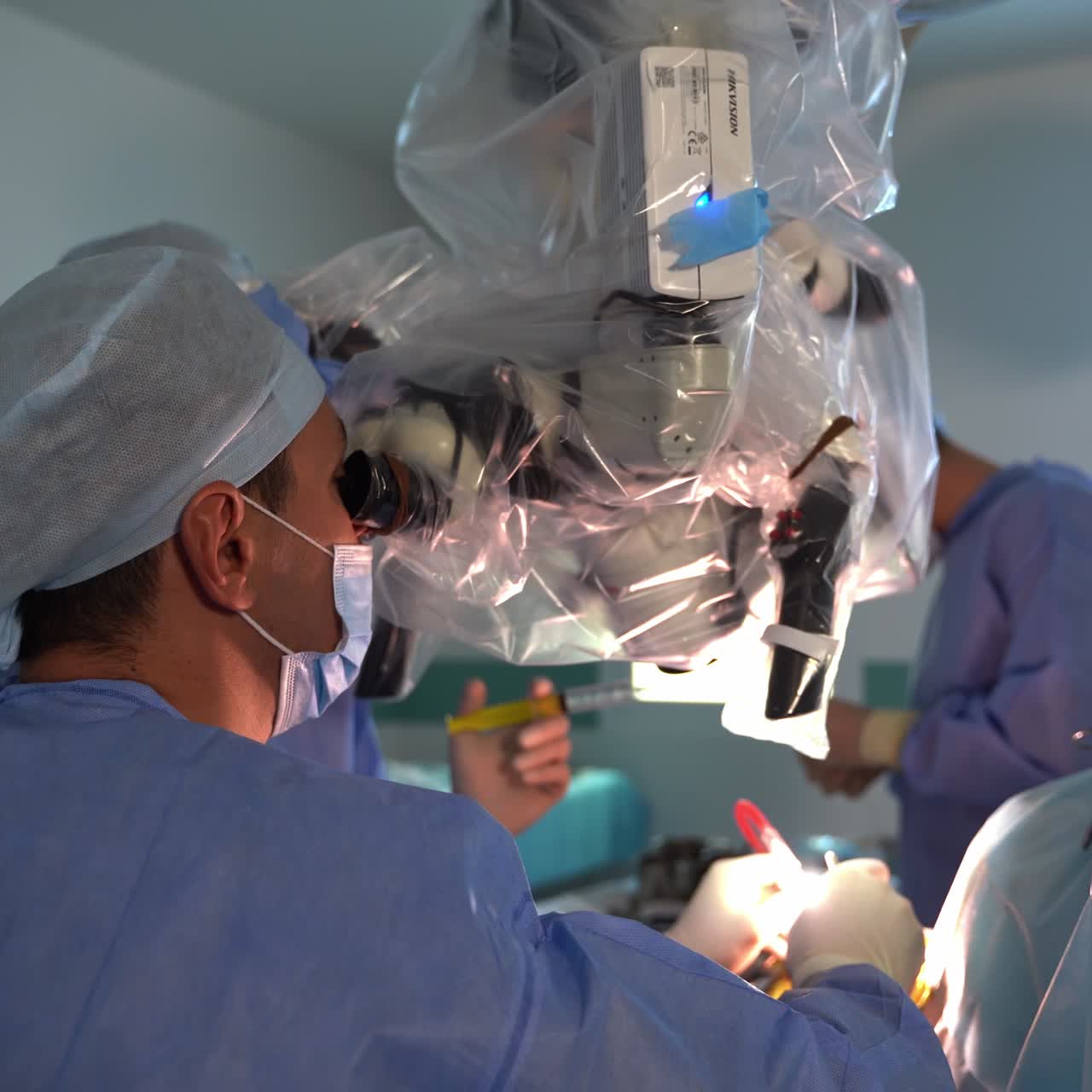 Male Caucasian doctor moves carefully with instruments looking into microscope. Surgeons cooperate during neurosurgical operation