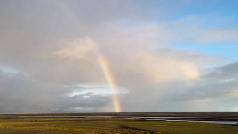 vibrant rainbow arching across icelandic plains with vast open skies, pov from car