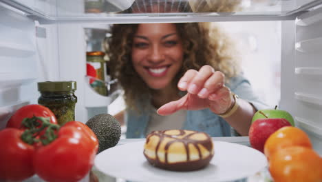vista mirando desde el interior del refrigerador cuando la mujer abre la puerta y alcanza la rosquilla no saludable